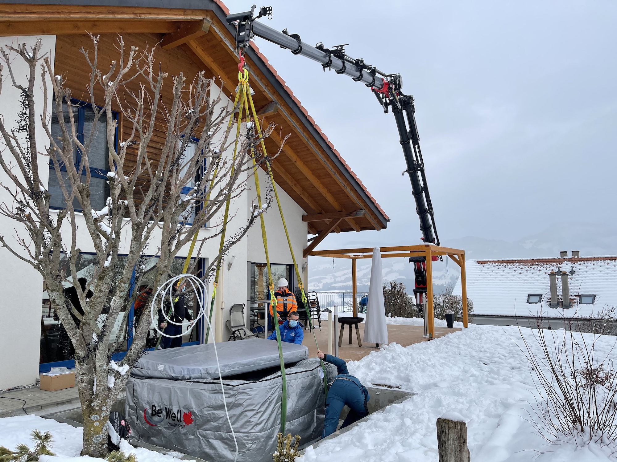 Livraison d'un spa Be Well par grue en plein hiver enneigé — le spa doit rester alimenté en électricité dès l'installation pour éviter le gel